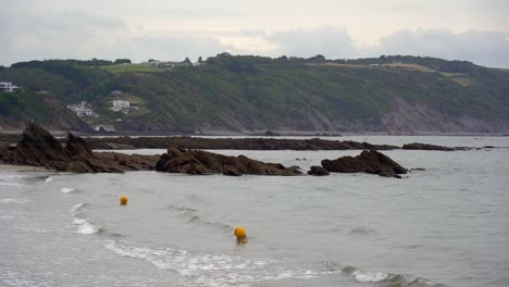 Las-Boyas-De-Advertencia-Amarillas-Suben-Y-Bajan-En-Las-Olas-De-East-Looe-Beach-En-Looe,-Cornualles,-Inglaterra,-Reino-Unido.