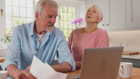 pareja de ancianos jubilados preocupados con computadora portátil mirando facturas en casa preocupados por el costo de la vida