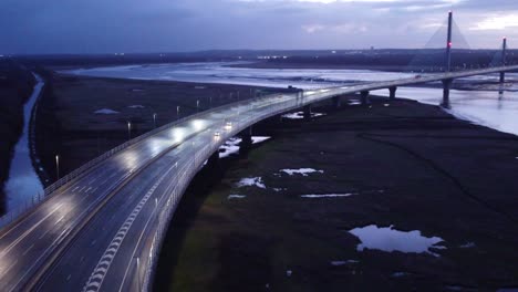 Aerial-view-Mersey-gateway-illuminated-freeway-bridge-overpass-lanes-early-morning-sunrise-forward-orbit-tilt-down-left