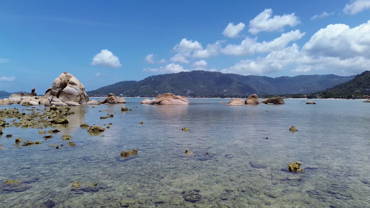 Aerial drone footage of Lamai Beach, Koh Samui, Thailand, showcasing rocky coastline, turquoise ocean water, lush green mountains, and scenic tropical island horizon under a clear sky