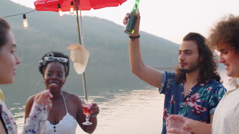 young friends dancing and toasting at lake party