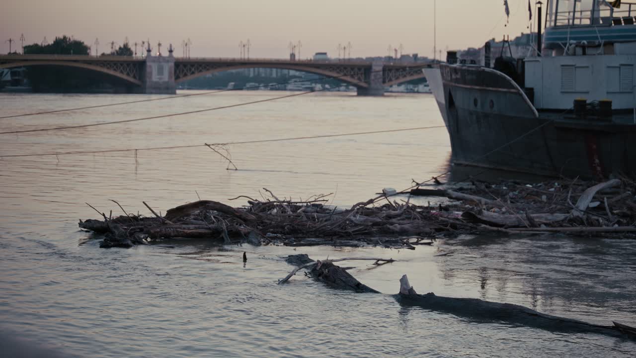 Debris floating in the river next to a docked boat in Budapest, bridge visible in the background
