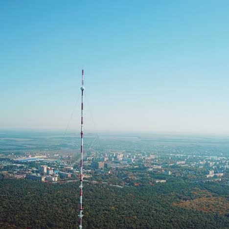 top of the telecommunication tower in red and white colours on the background of the cityscape and blue sky. camera motion up