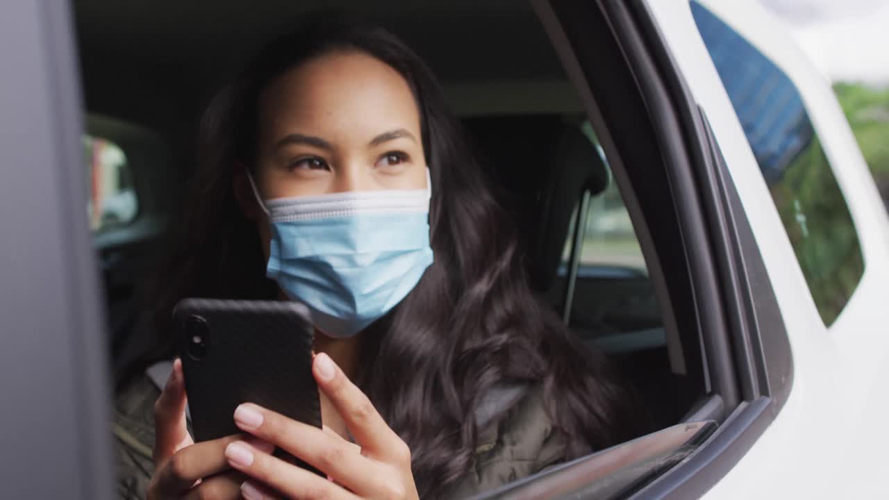mujer asiática con máscara facial usando un teléfono inteligente mientras está sentada en el coche