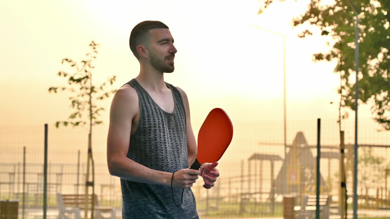 Man playing pickleball with a red racket at sunrise, after rain