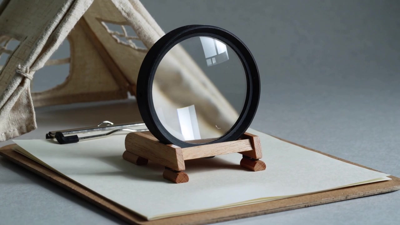 Panning camera moving right bringing magnifier closer to tabletop to reveal fabric tent and clip