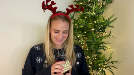 Young-Woman-On-Christmas-Video-Call-Opening-a-Present-Whilst-Talking-to-Camera