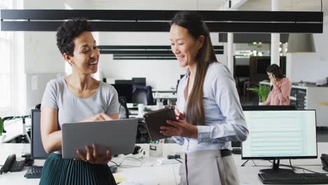 Happy-diverse-businesswomen-working-together-on-laptop-and-tablet-in-office