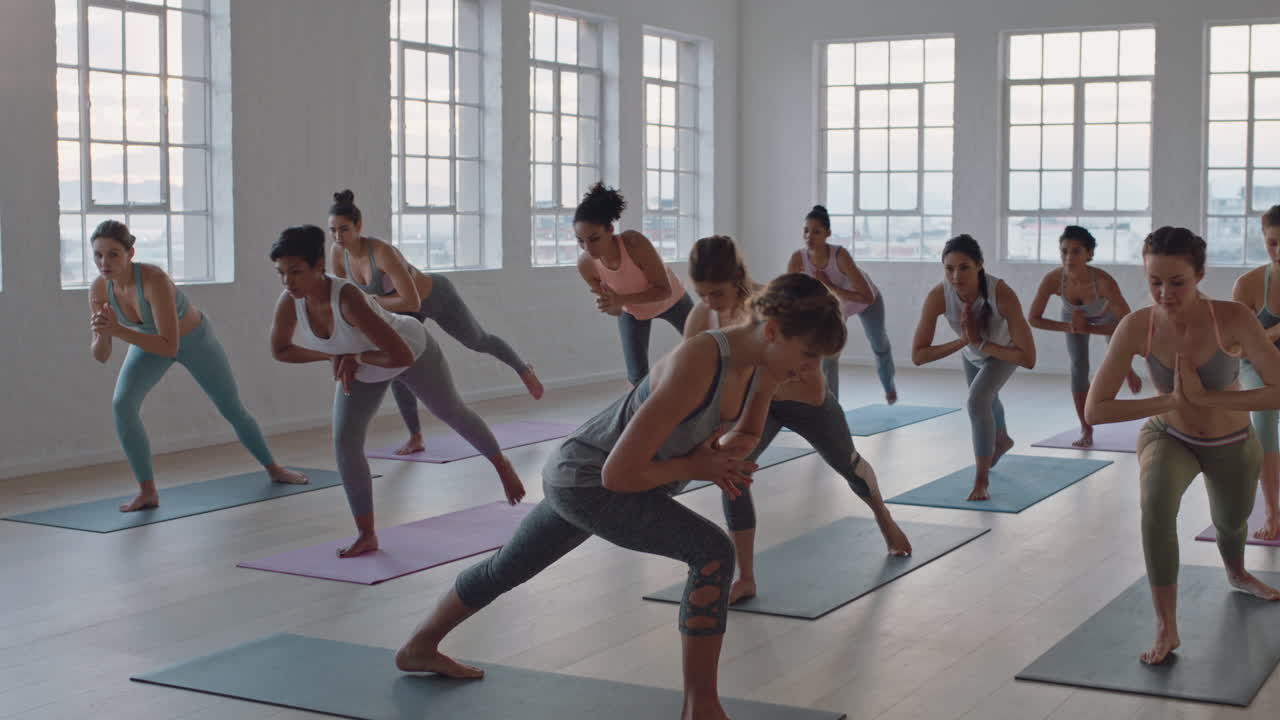 yoga-kurs mit gesunden frauen, die die krieger-pose praktizieren und das training im fitnessstudio genießen. der lehrer leitet die gruppenmeditation und lehrt die trainingshaltung bei sonnenaufgang