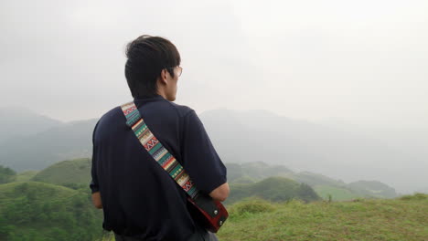 hombre asiático melodramático tocando el ukelele en la cima de una colina tropical del sudeste asiático