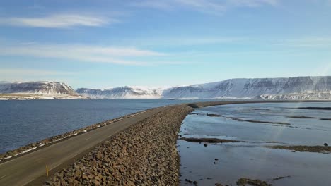 Aerial shot following along a rocky bridged road over an Icelandic lake