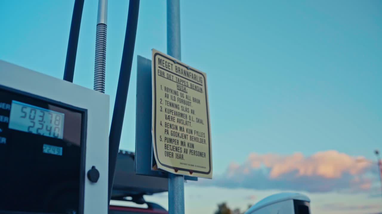 A Fuel Pump and Safety Sign Stand Quietly Under a Clear Sky at a Gas Station in Kokelv, Hammerfest, Finnmark, Norway - Close Up