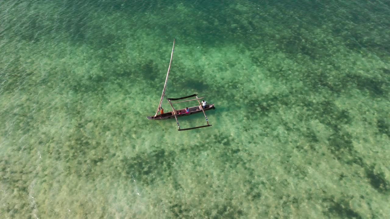Sailboat glides over clear turquoise water, viewed from above