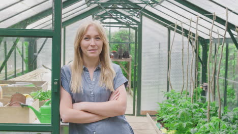retrato de una mujer cultivando verduras de pie en la puerta del invernadero y doblando los brazos