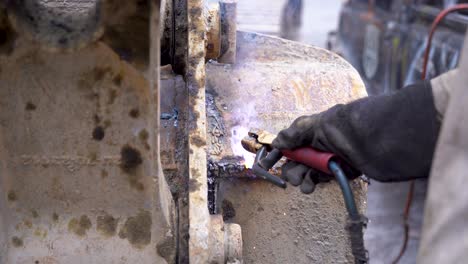 el arco del trabajador suelda piezas metálicas de la máquina y luego limpia las marcas de soldadura, cierra