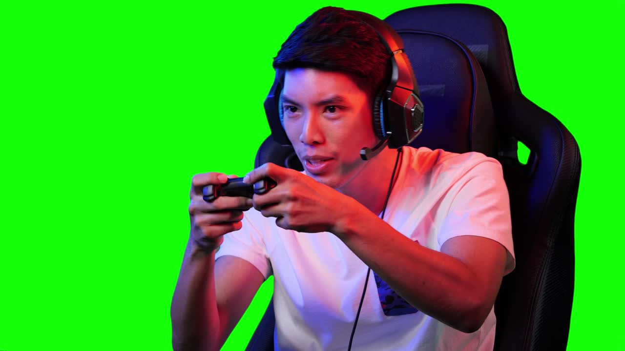 Gamer asiatico che gioca e guarda lo schermo. Uomo asiatico che controlla la console con i joystick. Bell'uomo che si diverte con un gioco digitale su sfondo verde o chroma key.