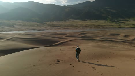 drone en órbita disparo de un tipo caminando en las grandes dunas de arena de colorado y las montañas