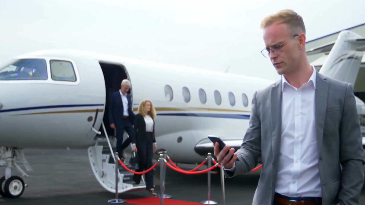Uomo d'affari che controlla lo smartphone vicino a un jet, presso una barriera di corda sul piazzale, con un grafico di stato animato.