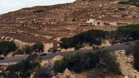 group riding quad bikes enjoying drive along mountain road in gozo, malta