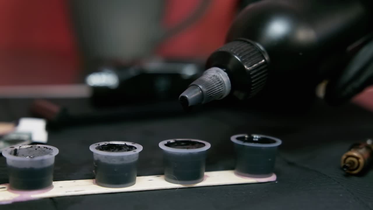 Tattoo artist dropping ink in slow motion in plastic cups with black colour at tattoo studio.