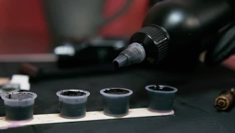 tattoo artist dropping ink in slow motion in plastic cups with black colour at tattoo studio.