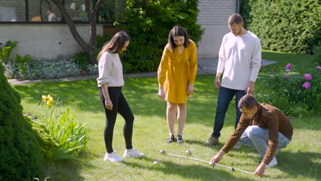 Caucasian-young-man-calculating-distance-between-petanque-balls-in-the-park-while-his-friends-looking-at-him