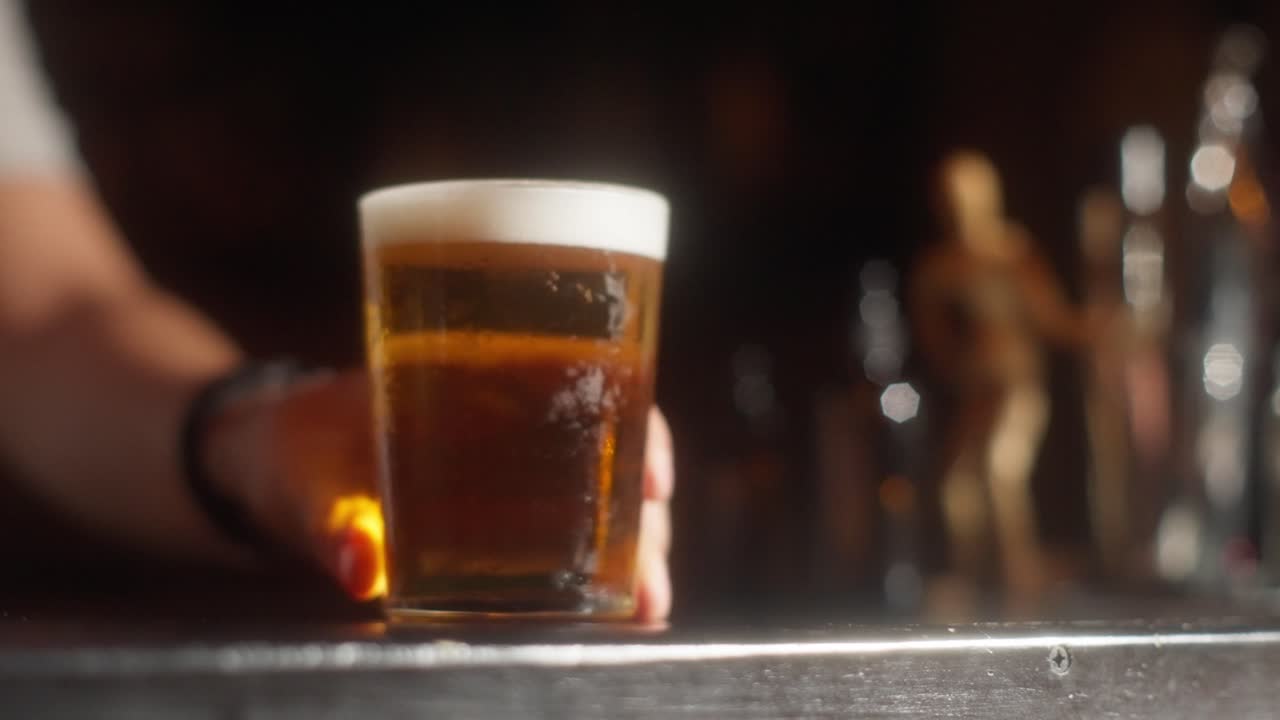 Glass of fresh beer in focus on bar table with beer dispenser in the background