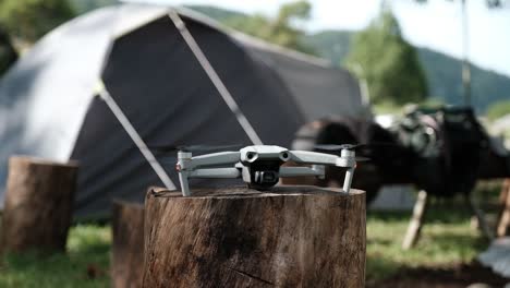 view of drone taking off from trunk in front of a tent in the camp, propellers start spinning, static