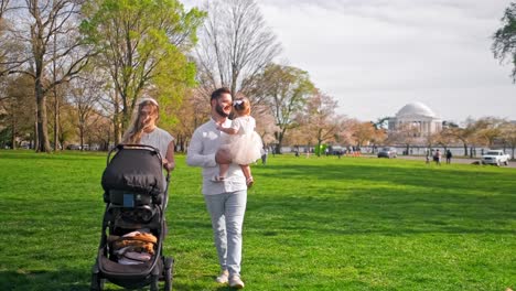 A happy family with a toddler and infant are walking at a park in Washington DC during the cherry blossom festival with the Thomas Jefferson Memorial in the background