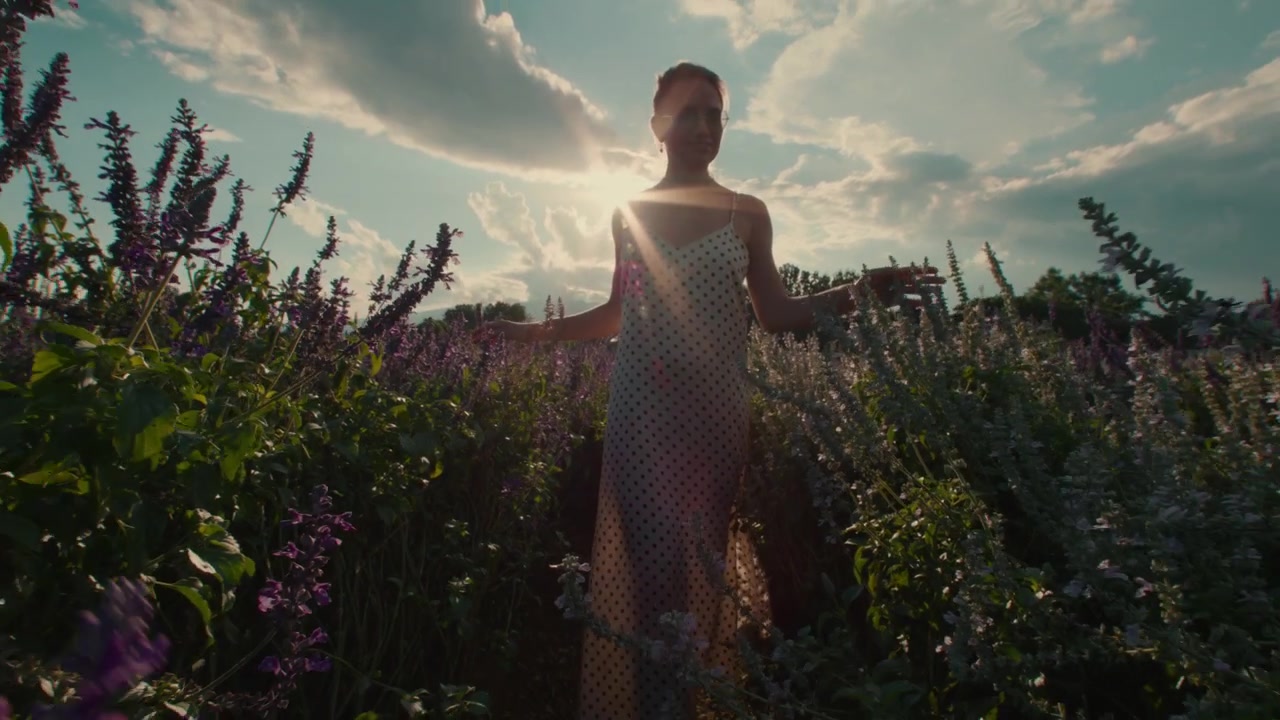 Young Woman Walking Through a Field of Purple Flowers at Sunset