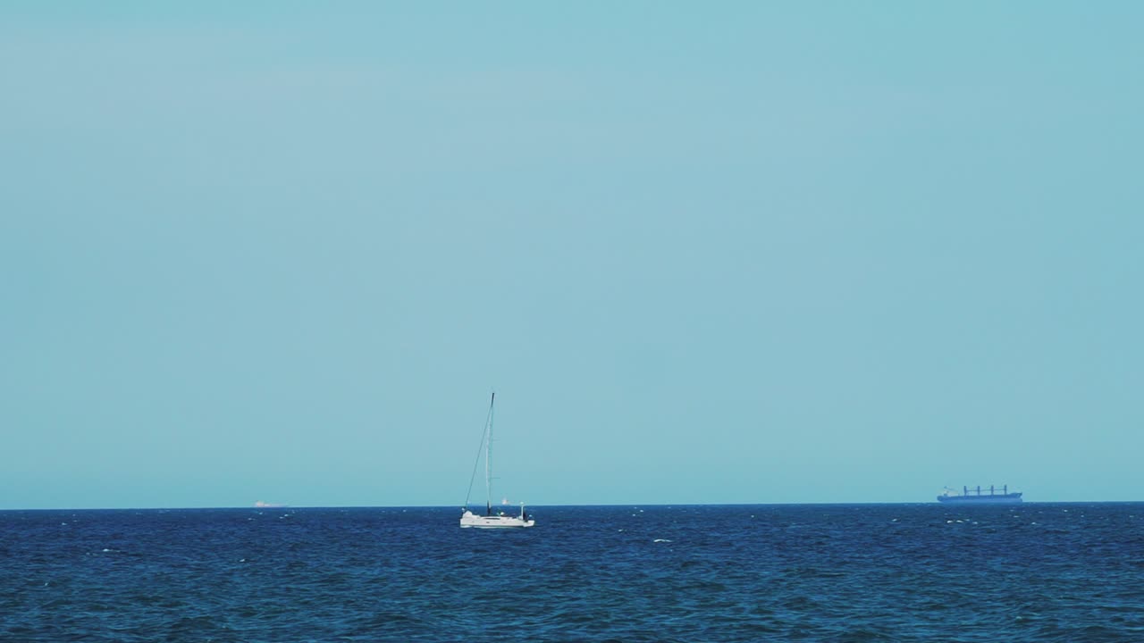 The yacht is under sail floats in the sea. On the horizon are seen cargo ships