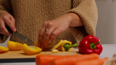 close up of woman at home in kitchen preparing healthy fresh vegetables for vegetarian or vegan meal slicing yellow pepper on board 2