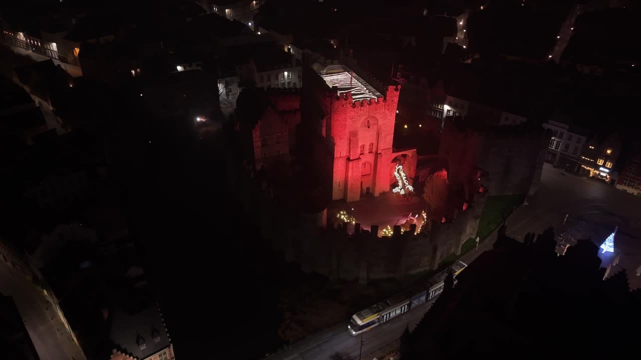 Orbiting footage of the Gravensteen Castle in Ghent illuminated in red during a dark night, creating a dramatic and atmospheric historic scene