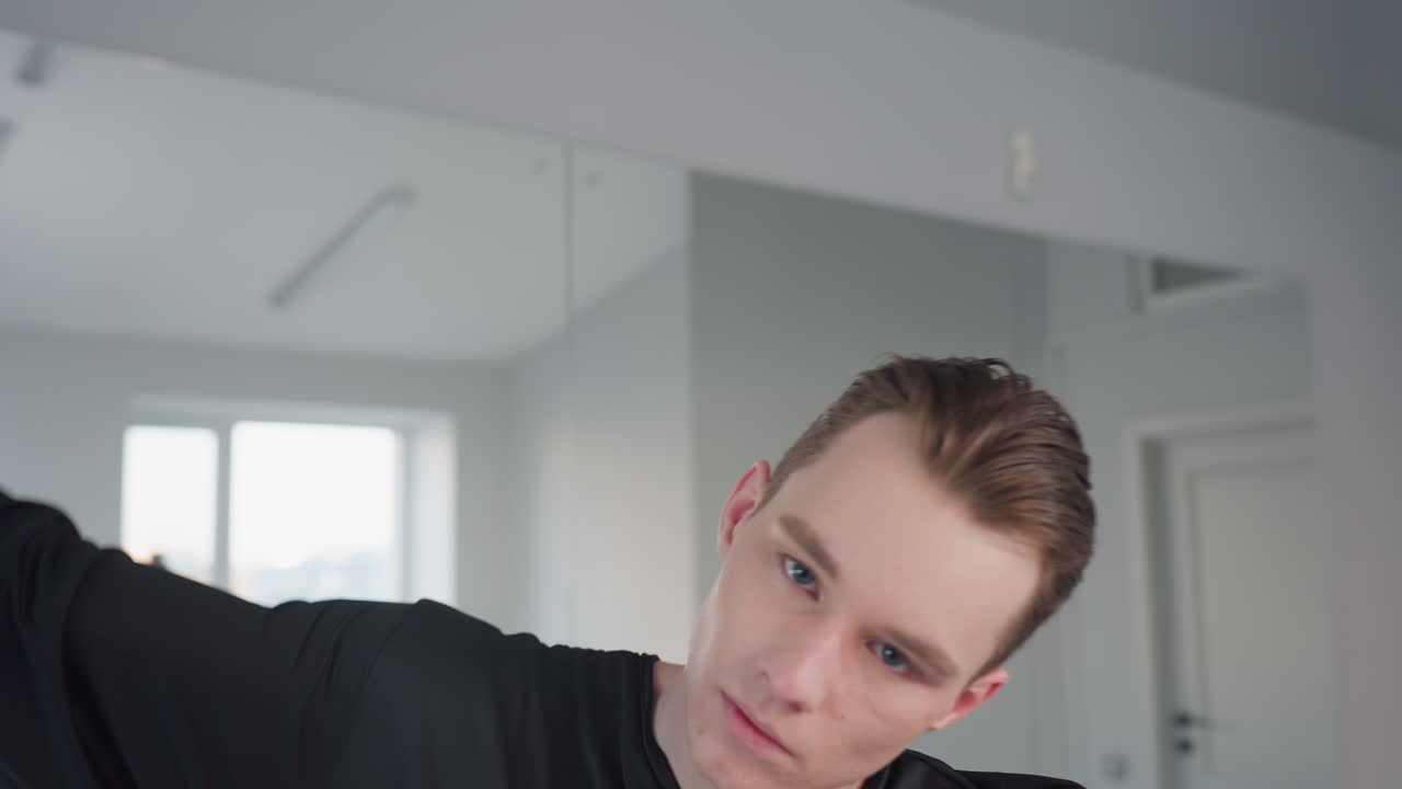 young man in black gloves gracefully removes hand from face, revealing poised expression and sleek hairstyle against mirrored studio backdrop