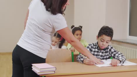 teacher checking copybook of pupil in classroom.