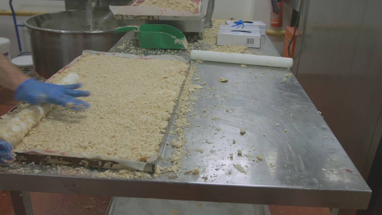 A worker at a stainless steel workspace prepares cake mix on a large tray which is then moved ready for the oven