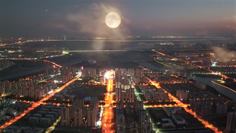 at night, the moon rises over the city，in the evening, city buildings light up and roads are illuminated by the lights