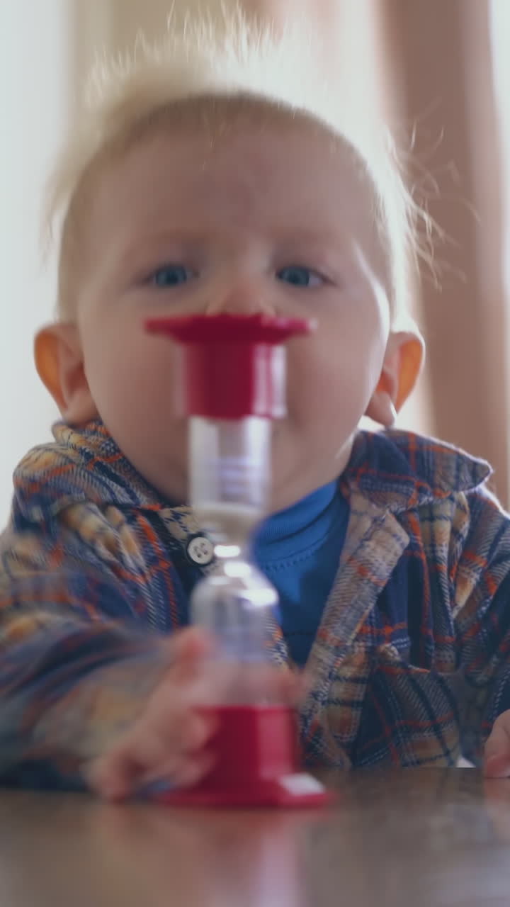 funny small son throws down sandglass from low wooden table and looks at mommy in light room close view