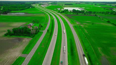 panoramic aerial shot of interstate 94 cutting through vibrant green farmlands in minnesota, freight trucks with rural landscape