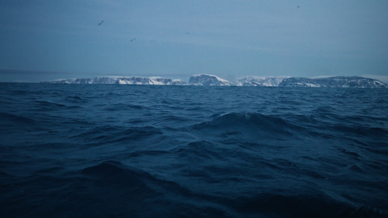 Fredde onde dell'Oceano Artico che si infrangono sotto un cielo pallido con la costa norvegese innevata in lontananza