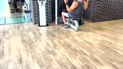 hombre concentrado sentado, realizando ejercicios de levantamiento de pesas con determinación en el gimnasio