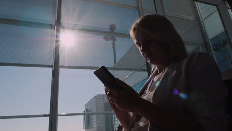 Una-Mujer-Espera-Su-Vuelo-En-La-Terminal-Del-Aeropuerto-Usando-Un-Teléfono-Inteligente