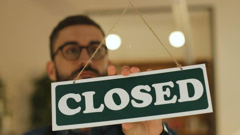 close-up view of young man turning over open" sign in his coffee shop window"