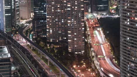 traffic and train travelling in tokyo city at night passing by condominiums and hotel from seaside top observatory of world trade center in tokyo, japan