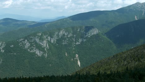 green mountain range with granite sits above treetops as the camera passes by, creating a sense of depth