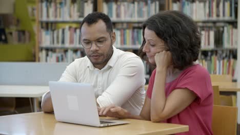 smiling students discussing something while working with laptop