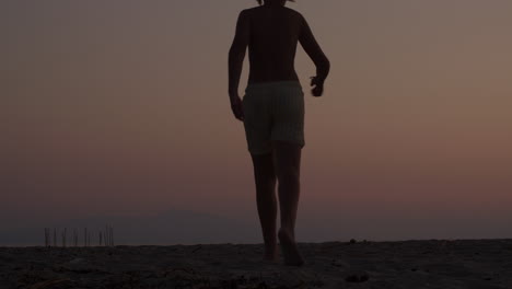 teenage boy walking into sunset on beach