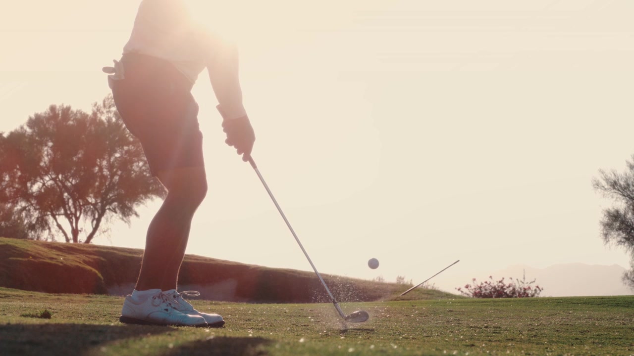 Un golfista esegue un chip dritto verso il sole al tramonto mentre la luce si irradia attorno alla silhouette, ripreso al rallentatore, adatto a promo drammatici di golf e lifestyle.