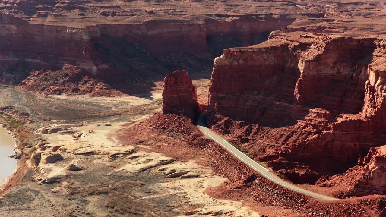 Una prospettiva da drone segue una strada asfaltata che si snoda tra imponenti pareti di arenaria. Questa vista in 4K cattura la scala e l'isolamento di un remoto percorso di viaggio avventuroso.