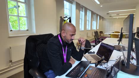 un individu est assis à un bureau dans un bureau moderne, avec des verres dans la bouche et secouant la tête de frustration